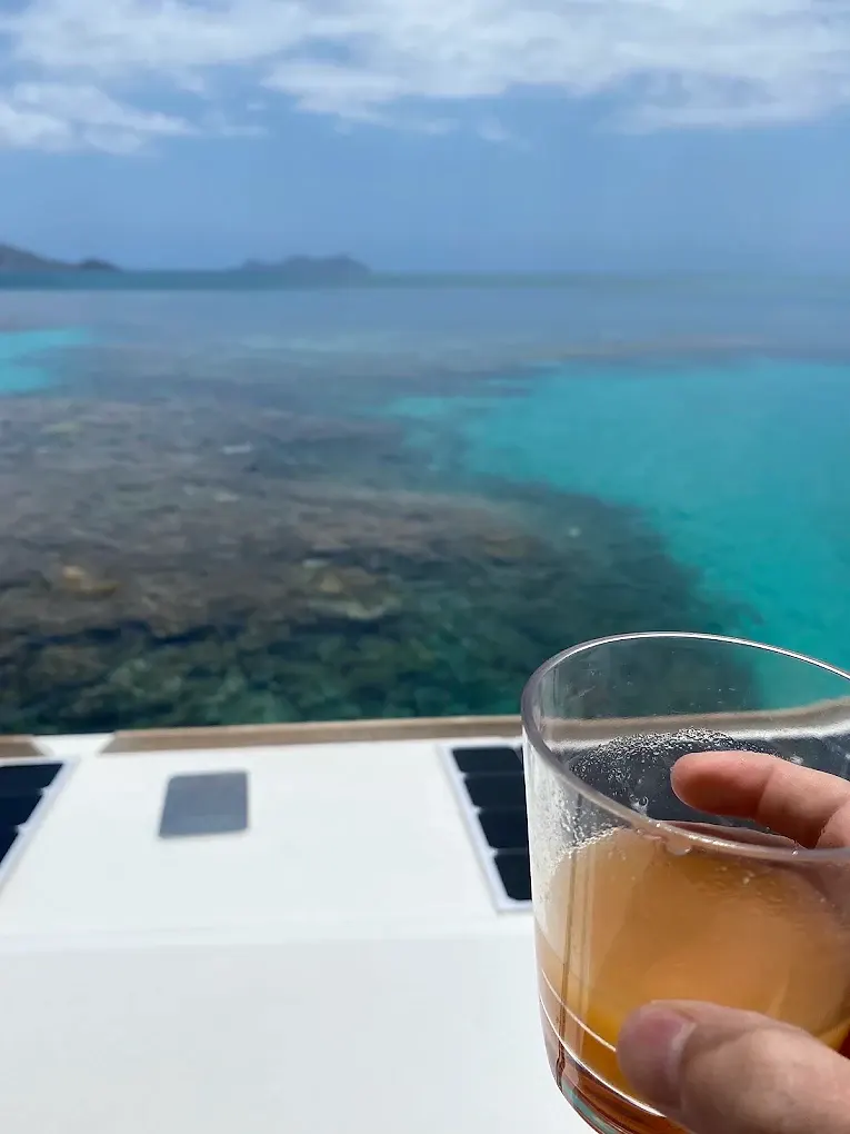 Un verre à la main sur le pont, le récif en arrière-plan