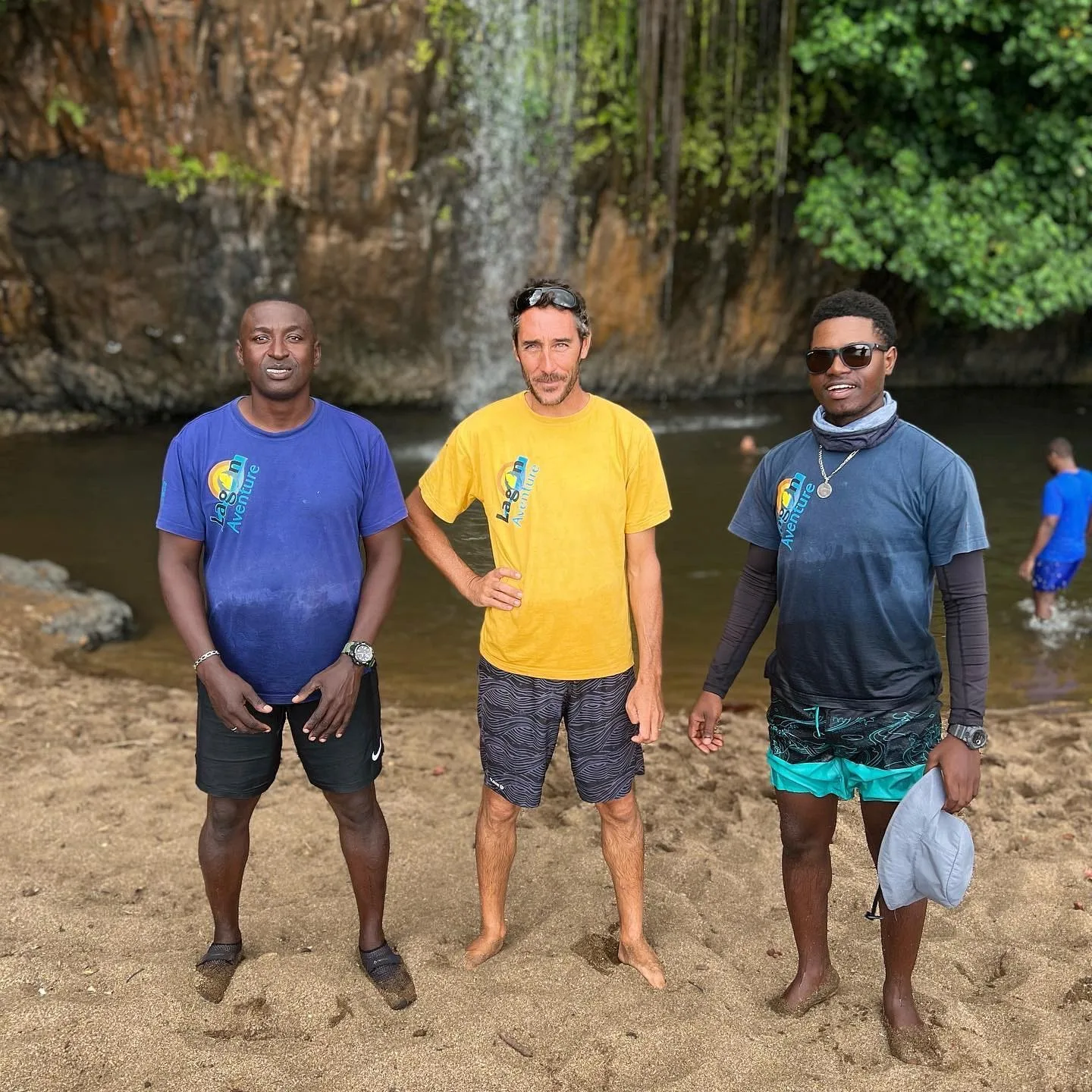 Trois membres de l’équipage en t-shirt Lagon Aventure, sur la plage devant la falaise