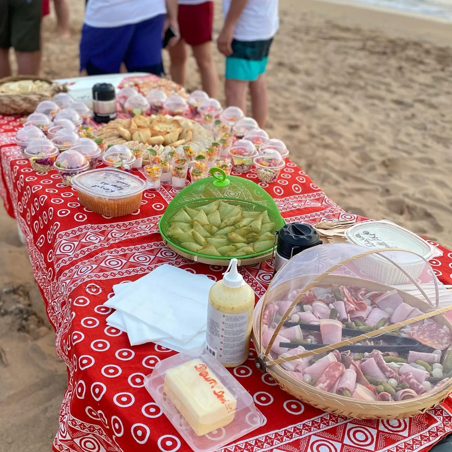 La table dressée sur le sable de l’îlot : plats couverts, nappe rouge à motifs, passagers autour